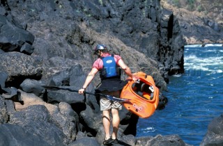 Canoeist carries his canoe over rocks on the Zambezi River, Zambia