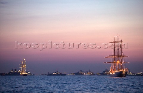 Square riggers at anchor with Trafalgar 200 warship fleet in background at sunset