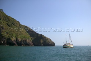 A converted fishing trawler at anchor by a headland