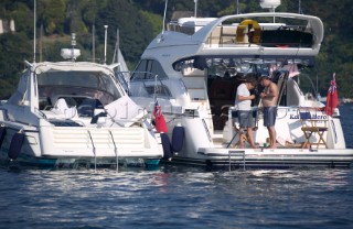 Large cruising powerboats with British ensigns moored in Salcombe Harbour. Two men prepare a fishing line.