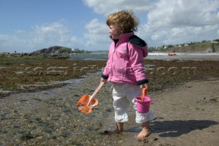 Little girl in pink jacket with bucket and spade on sandy beach