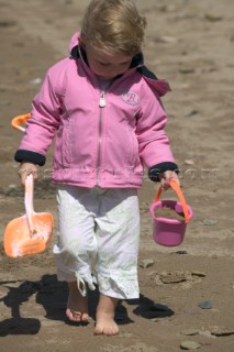 Little girl in pink jacket with bucket and spade on sandy beach