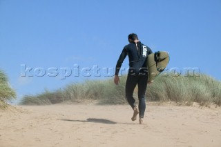 Surfer walking up beach with board under arm