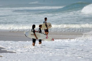 Three surfers with their boards looking out at the surf