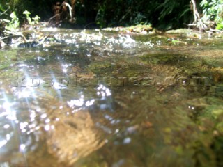 Low down waterline view of a river and stream with moss growing on the rocks and reflections and highlights from the sun