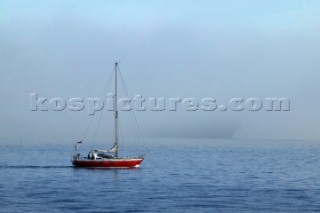 Cruising yacht motoring in fog on calm sea as large container ship approaches on a collision course