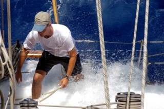 Antigua Classic Yacht Regatta April 2006. Part of sequence of crew member on Aschanti IV working on leeward side as wave comes crashing over side of boat to submerge  him as he holds on to a line