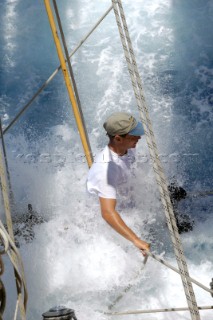 Antigua Classic Yacht Regatta April 2006. Part of sequence of crew member on Aschanti IV working on leeward side as wave comes crashing over side of boat to submerge  him as he holds on to a line