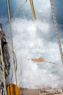 Antigua Classic Yacht Regatta April 2006. Part of sequence of crew member on Aschanti IV working on leeward side as wave comes crashing over side of boat to submerge  him as he holds on to a line