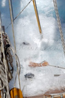 Antigua Classic Yacht Regatta April 2006. Part of sequence of crew member on Aschanti IV working on leeward side as wave comes crashing over side of boat to submerge  him as he holds on to a line