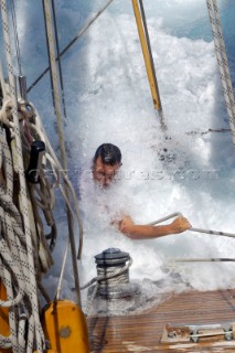 Antigua Classic Yacht Regatta April 2006. Part of sequence of crew member on Aschanti IV working on leeward side as wave comes crashing over side of boat to submerge  him as he holds on to a line