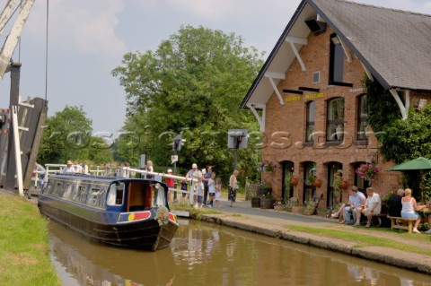 People on narrow boat passing through Wrenbury lift bridge outside the Dusty Miller pub on the Llang