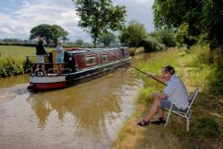 Narrow boat passing man fishing on the Llangollen canal,near Ellesmere,Shropshire,England,UK.July 2006.