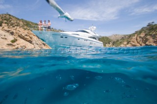 A seagull peruses a menu of fish from just above the waterline watched by three people on standing on the bow of a power boat