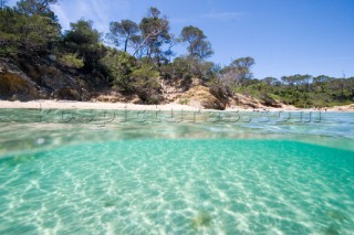 The shore as seen from a camera half-submerged in clear shallow water