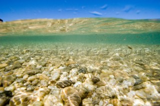 A shallow clear stream tumbles over a bed of pebbles under a sunny blue sky