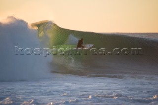 A surfer on a large breaking wave at dusk