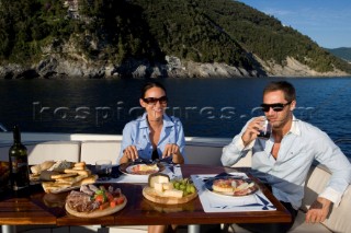 Lifestyle couple dining and eating dinner or lunch onboard a Vicem 72 classic motor yacht Model Released.