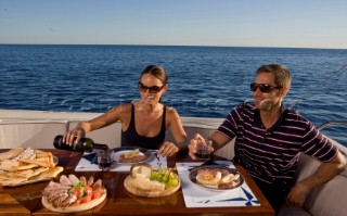 Lifestyle couple dining and eating dinner or lunch onboard a Vicem 72 classic motor yacht Model Released.