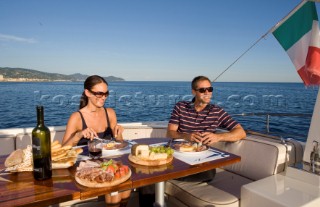 Lifestyle couple dining and eating dinner or lunch onboard a Vicem 72 classic motor yacht Model Released.