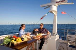 Lifestyle couple dining and eating dinner or lunch onboard a Vicem 72 classic motor yacht Model Released.