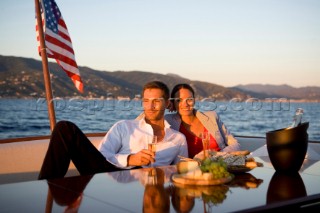 Lifestyle couple having drinks and coctails onboard a Vicem 72 classic motor yacht in the sunset Model Released.