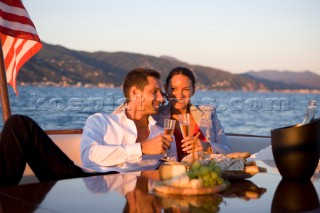 Lifestyle couple having drinks and coctails onboard a Vicem 72 classic motor yacht in the sunset Model Released.