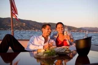 Lifestyle couple having drinks and coctails onboard a Vicem 72 classic motor yacht in the sunset Model Released.