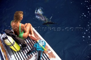 Sexy girl female model Jilly Johnson in green swimsuit onboard powerboat preparing to snorkel and scuba dive with tanks watching fish on the surface