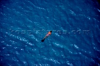 Lone female girl snorkelling on bright blue water in solitude