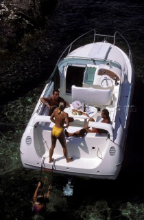 Sexy girl leaving the water after swimming onto the stern of an anchored powerboat watched by a man