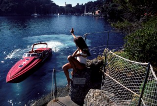 Romantic guy arriving in a fast red powerboat to collect sexy beautiful girl female model in a white swimsuit