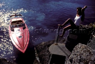 Romantic guy arriving in a fast red powerboat to collect sexy beautiful girl female model in a white swimsuit