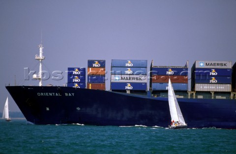 Sailing boat in shipping lane sailing passed container ship