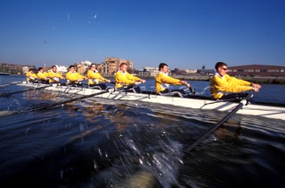 A team of rowers wearing yellow uniform clothing  in a skull on the River Thames