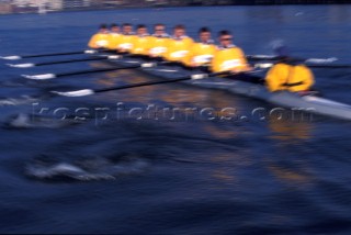 A team of rowers wearing yellow uniform clothing  in a skull on the River Thames