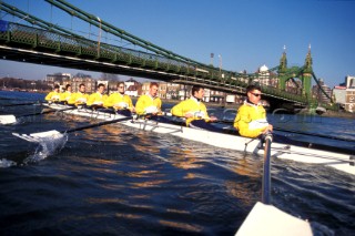 A team of rowers wearing yellow uniform clothing  in a skull on the River Thames