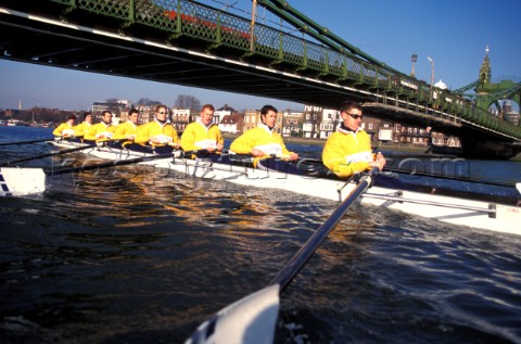 A team of rowers wearing yellow uniform clothing  in a skull on the River Thames