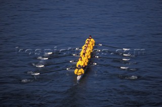 A team of rowers wearing yellow uniform clothing  in a skull on the River Thames