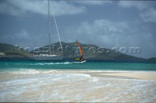 Woman standing on a sailboats bow waving at a windsurfer