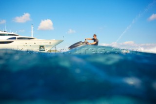 Man jet skiing in the mediterranean sea near a superyacht.