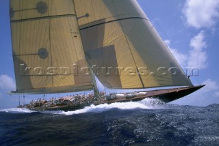 130 J-Class sloop, an elegant classic yachts, sails in a regatta under blue sunny skies.