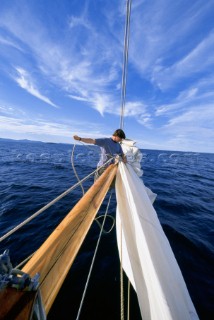 The bowman on board the classic schooner,  Wendameen, furls the jib at the end of the bowsprit after a sail on Penobscot Bay, Maine.