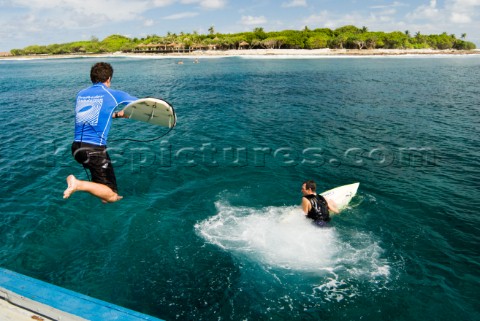 Surfers leaping into the ocean off a dhoni traditional Maldivian boat at the start of a surf session