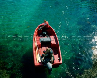 A couple sit aboard a little red speed boat on beautiful crystal clear water. The Lofotens, Arctic Circle, Norway Jun-Jul 2008