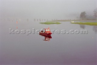 A red lobster boat in the fog at high tide in the Cape Neddick river in York, Maine.