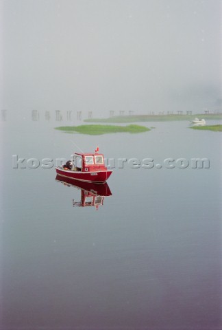 A red lobster boat in the fog at high tide in the Cape Neddick river in York Maine