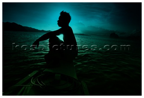 A fisherman sits on the edge of his boat as the sun rises amongst the rock formations that sit in th