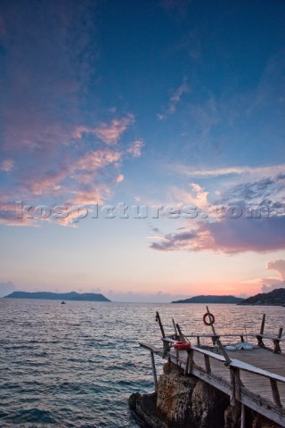 A wooden dock sticks out into the Mediterranean Sea at sunset in Kas Turkey