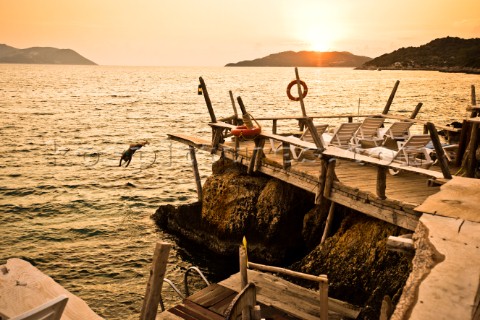 A girl dives off a wooden dock into the Mediterranean Sea at sunset in Kas Turkey